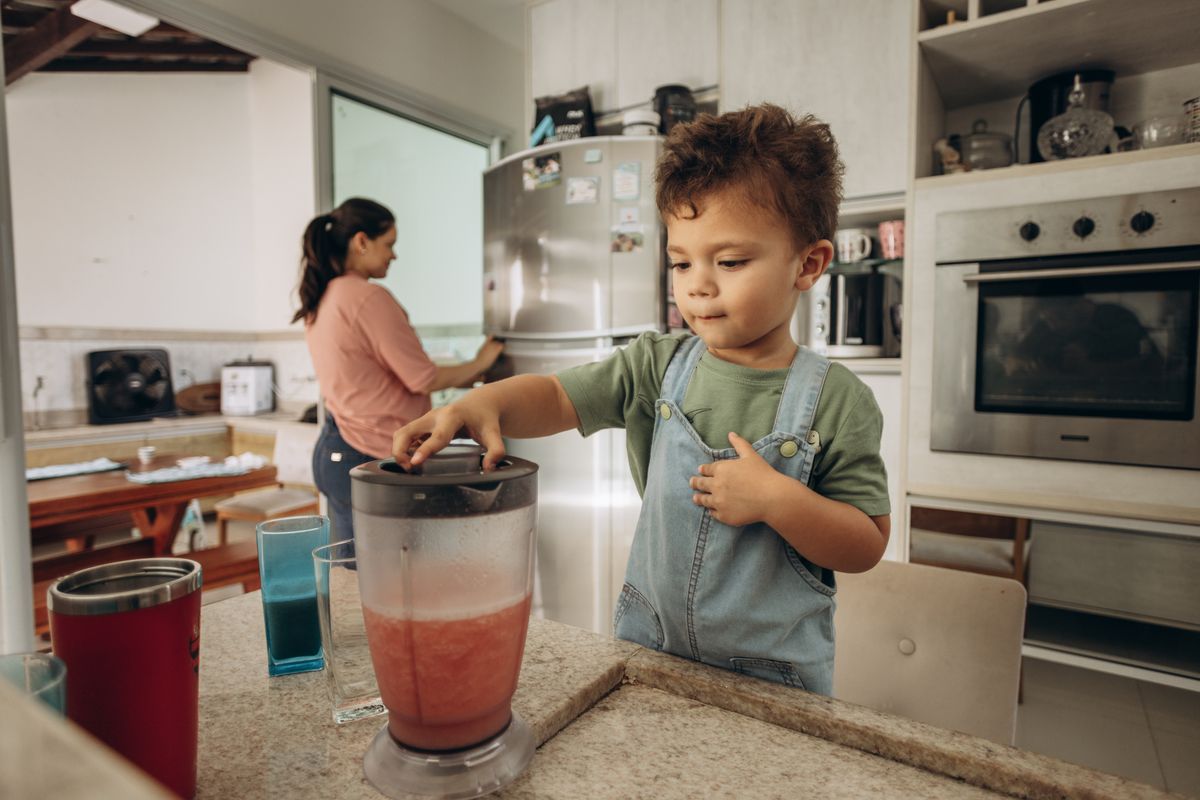 Child making a smoothie with a blender in the kitchen